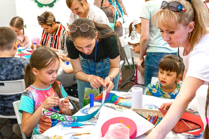 Children and teachers creating layered paper crafts with scissors, glue, markers, and colorful materials