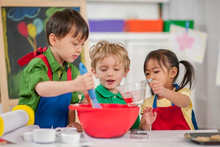 Three children measuring, pouring, and mixing ingredients together