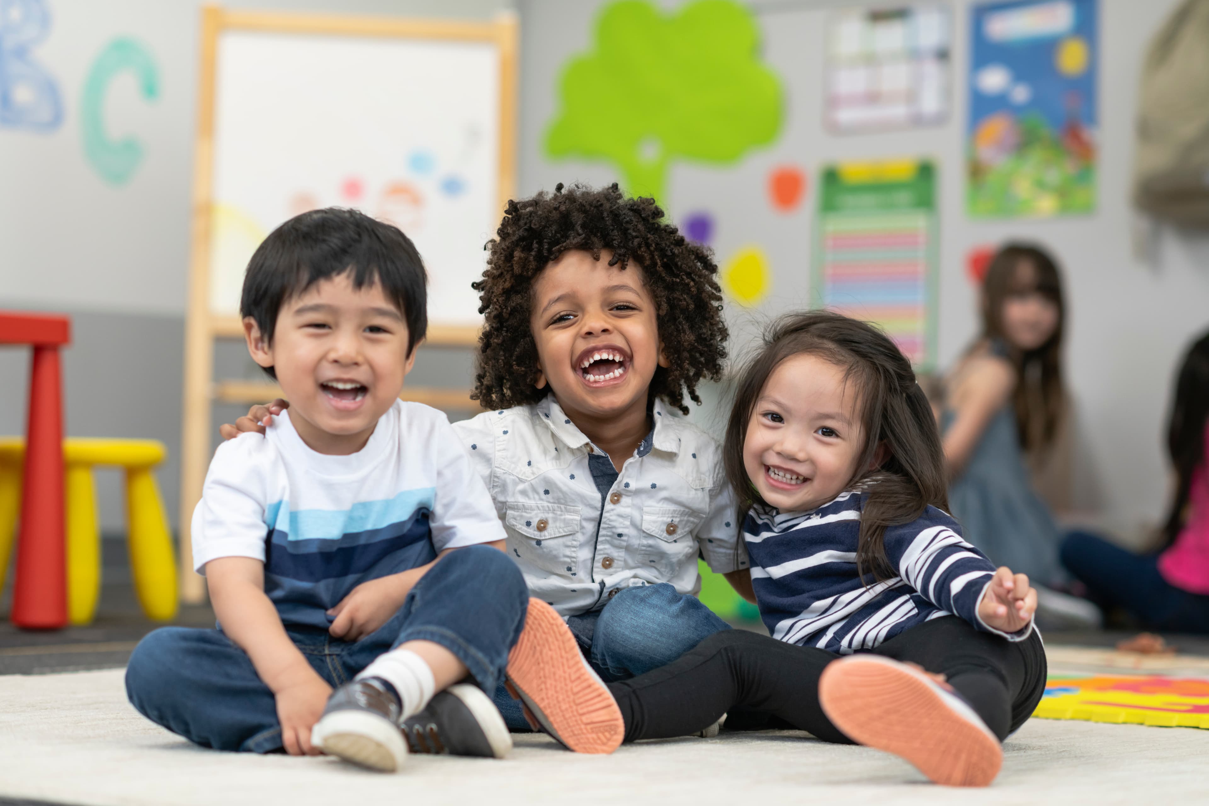 Three children laughing together in a bright classroom