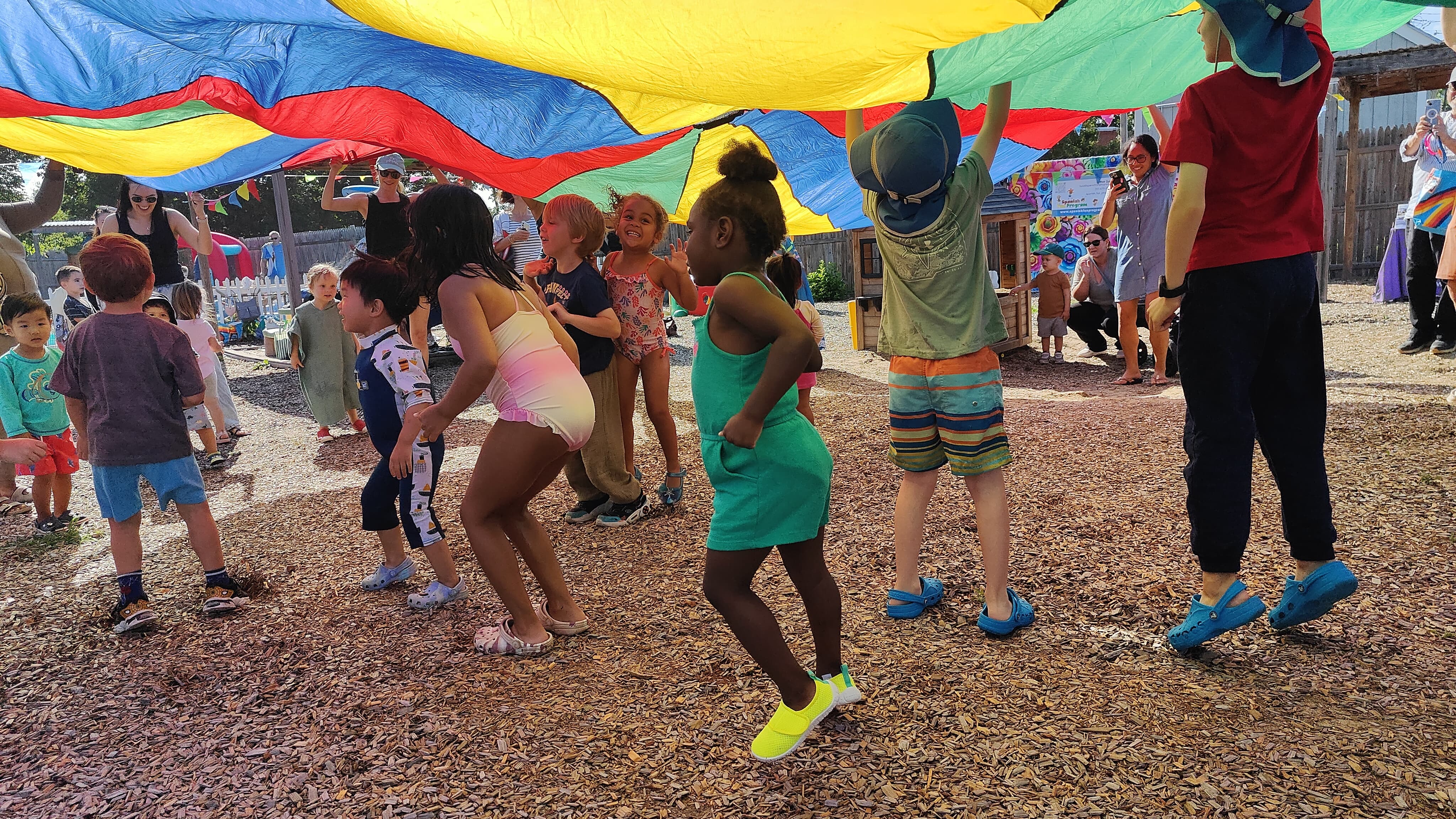 Children moving and playing together beneath a colorful parachute outdoors